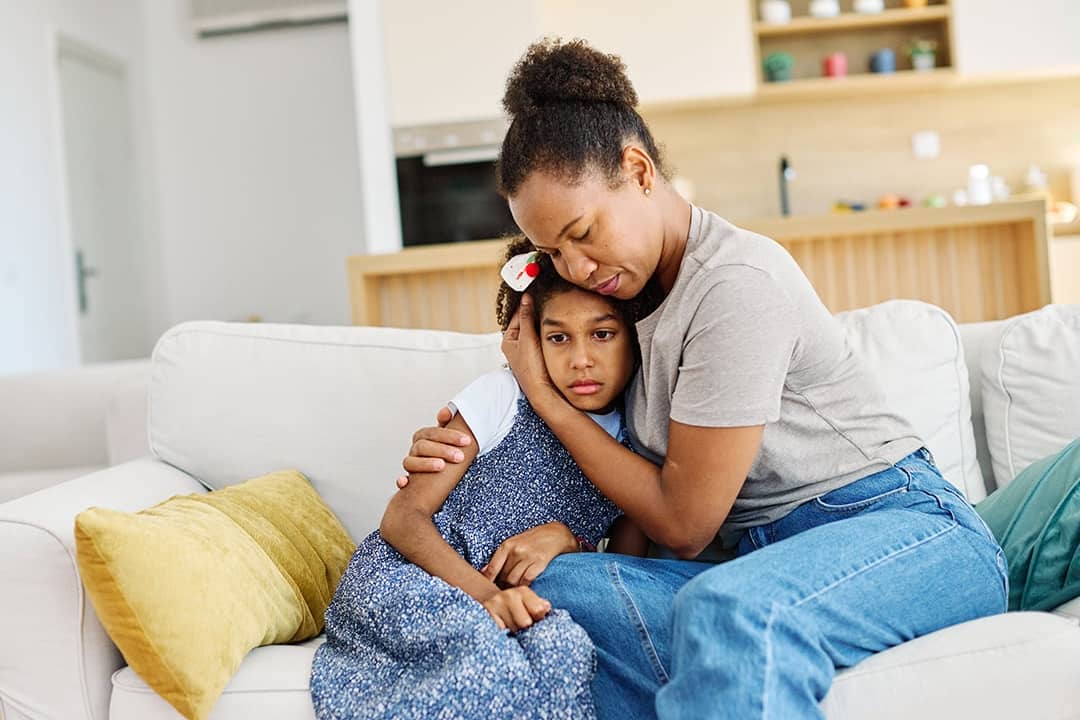 Mother embraces daughter on a couch at home while comforting her after a difficult day